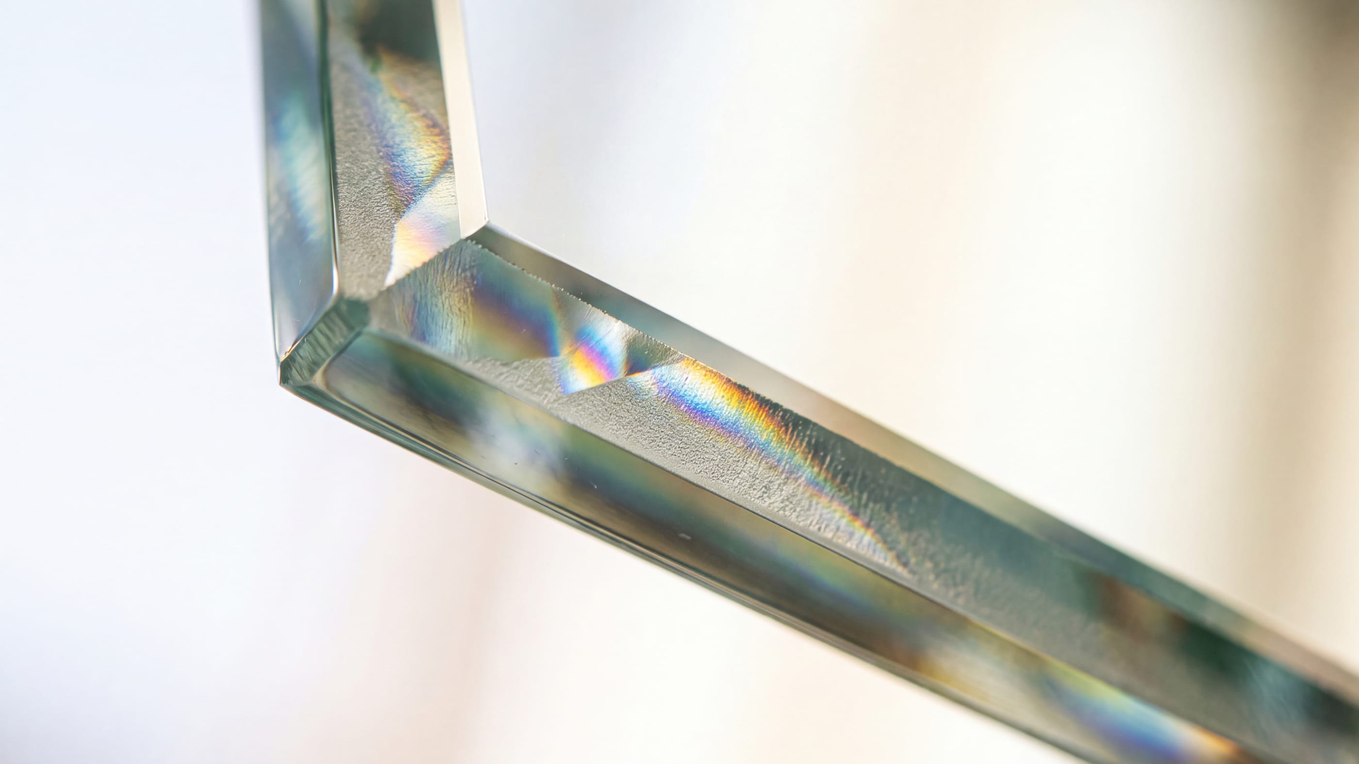 Nahaufnahme einer schrägen Kante aus klarem Glas vor hellem Hintergrund, an der sich das Licht in einer feinen matten Fläche bricht.