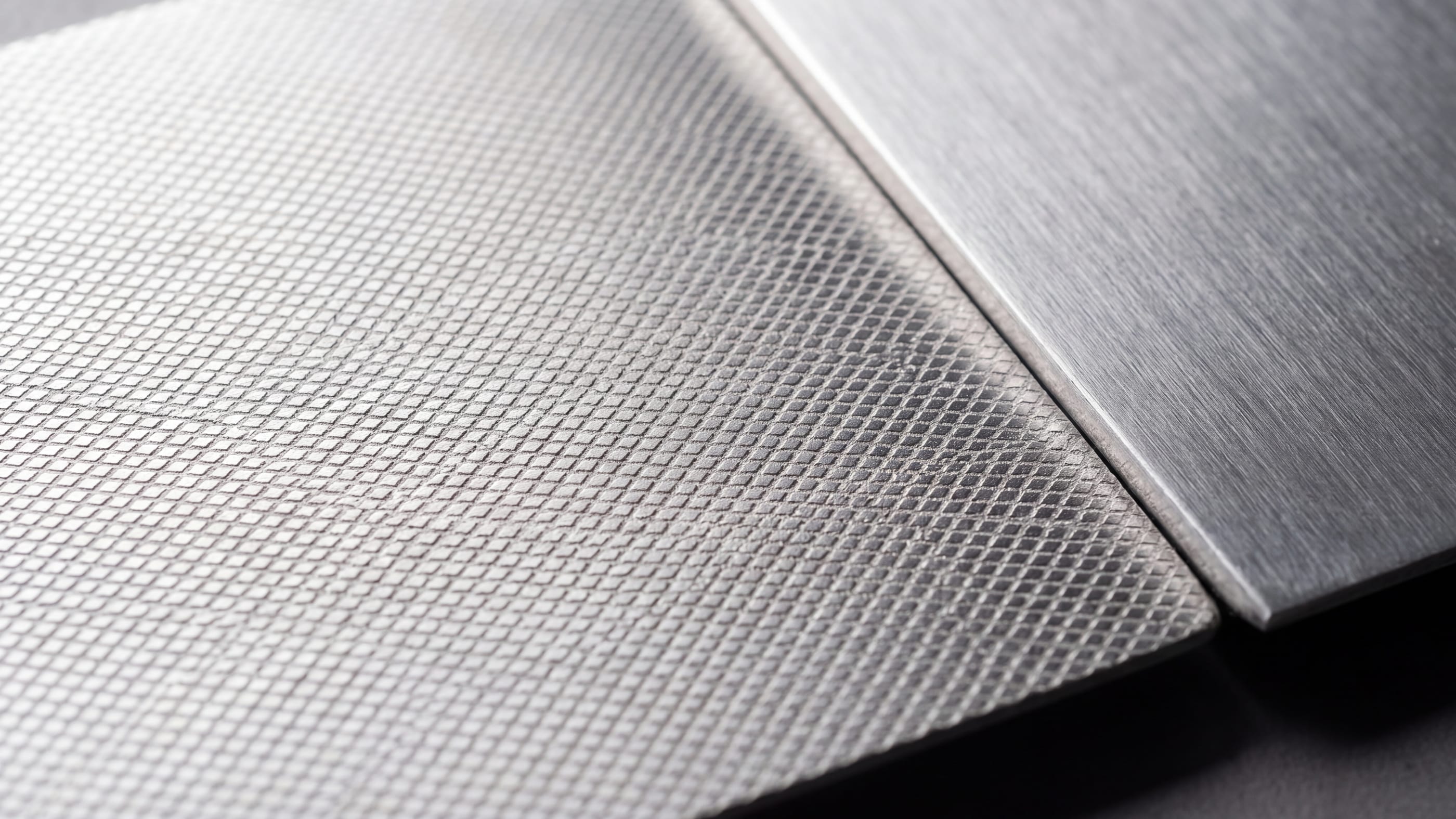 Zwei gebürstete Aluminiumplatten nebeneinander: die linke trägt ein flächig eingelassenes Rautenmuster, die rechte ist unbehandelt