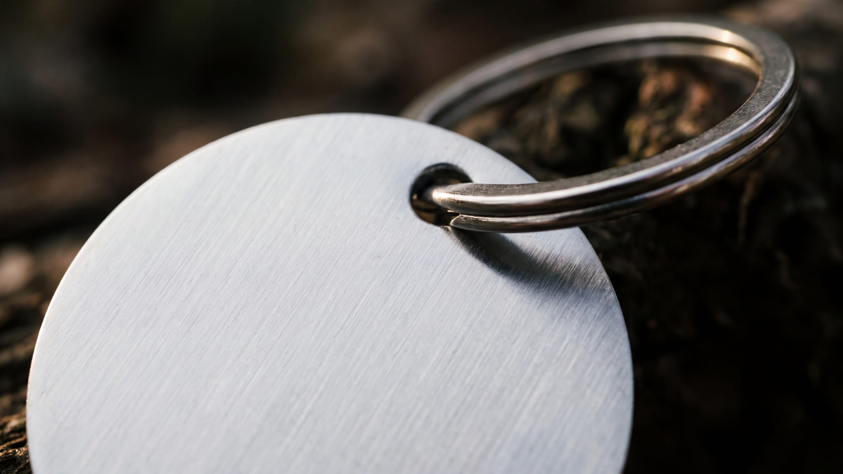 Makroaufnahme eines runden unbedruckten Metall-Schlüsselanhängers mit stabilem Spaltring, im Streiflicht sind gebürstete Struktur und Verbindungsstelle sichtbar.